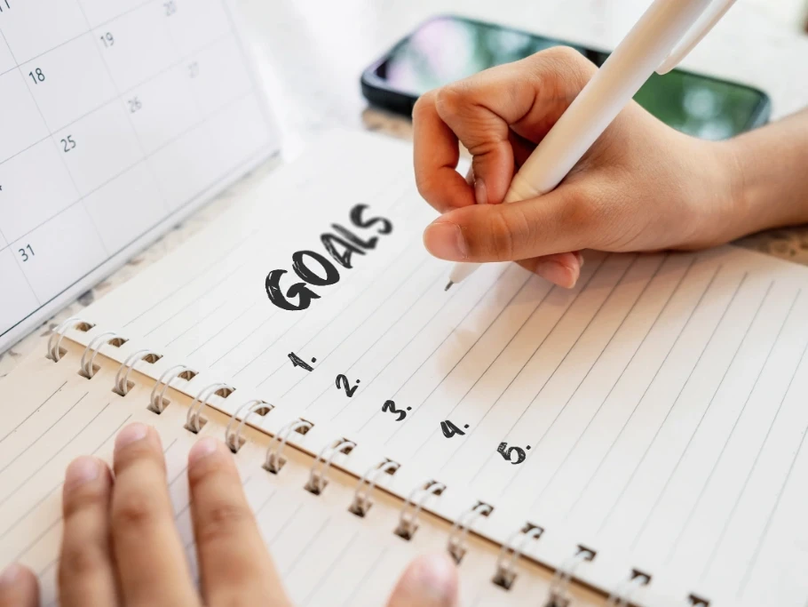 Hand writing goals in a notebook beside a calendar, representing a blog about new years resolutions by Gildeas Solicitors.