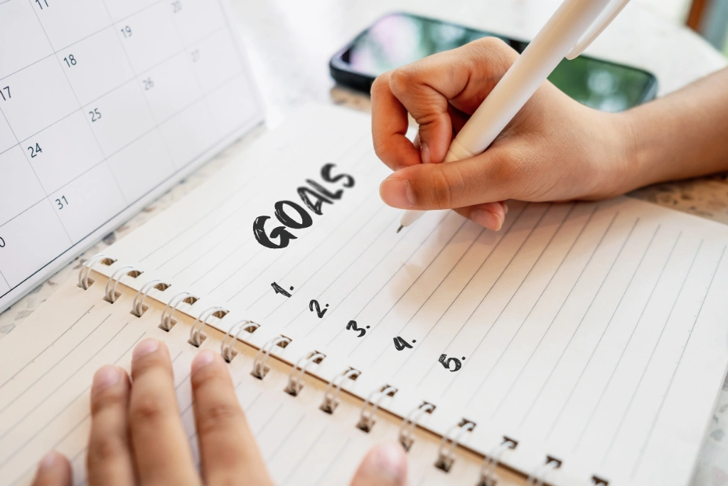 Hand writing goals in a notebook beside a calendar, representing a blog about new years resolutions by Gildeas Solicitors.