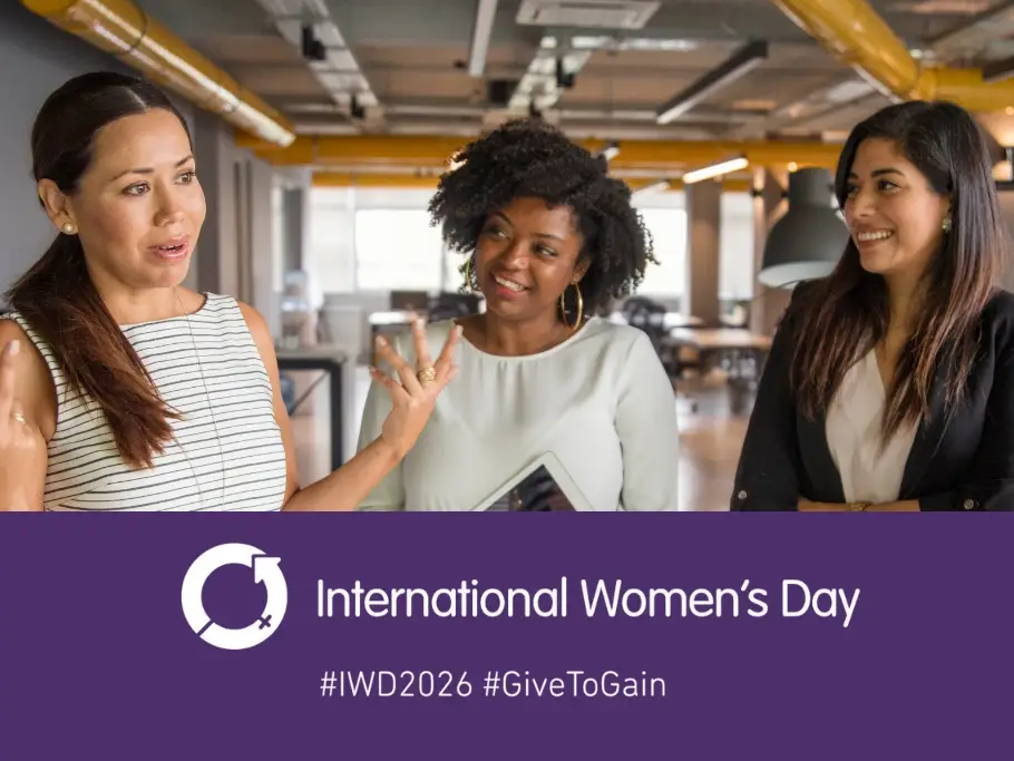 Three professional women standing together and smiling in an office setting, above a purple International Women’s Day banner featuring the IWD symbol and the words International Women’s Day with hashtags IWD2026 and GiveToGain, used by Gildeas Solicitors for International Women’s Day 2026.