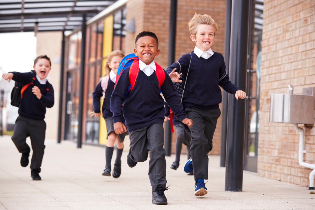 Children running towards school during the back to school period as traffic passes nearby. This could lead to contributory negligence